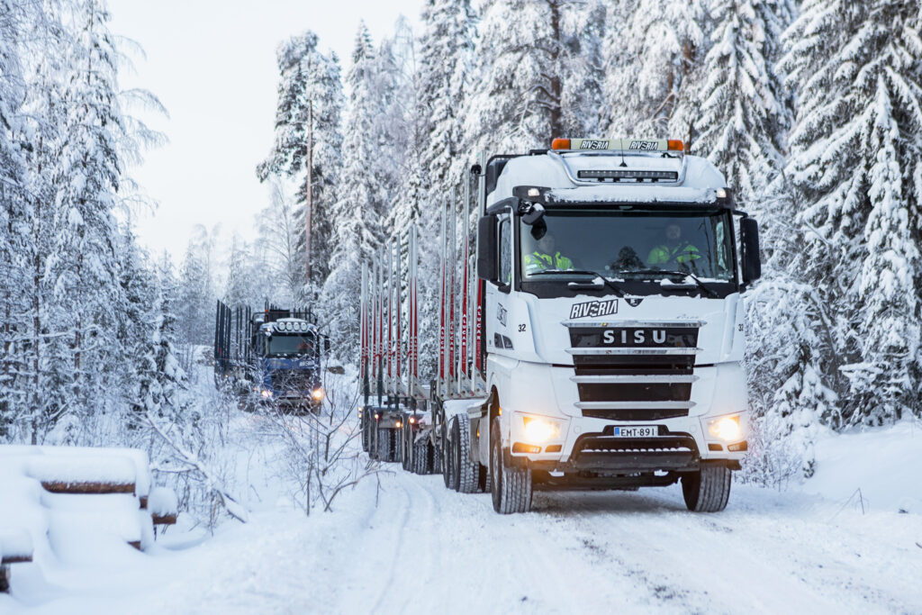Kaksi puutavara-autoa ajaa peräkkäin lumisella tiellä.